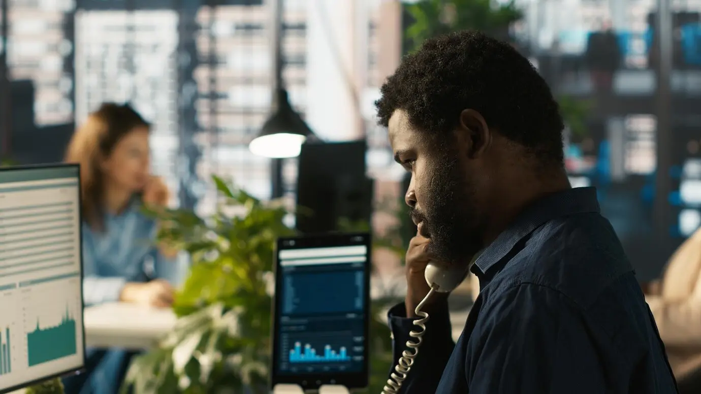 Nahaufnahme eines Angestellten im Büro, der ein Festnetztelefon benutzt, um mit einem Kunden zu sprechen.